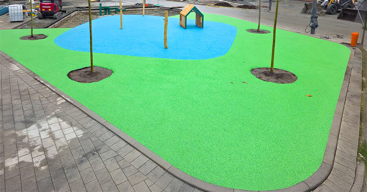 Fertige Spielfläche mit grün-blauer Fallschutzbeschichtung und Bäumen